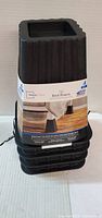 Stack of four black plastic bed risers with label
