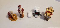 Four small Christmas resin figurines lined up on white background