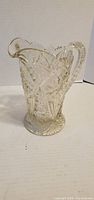 Front view of clear pressed crystal pitcher showing floral pattern and scalloped rim