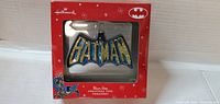 Front view of ornament in box showing Batman logo glitter details