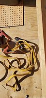 Coiled yellow booster cables with red and black clamps on plywood surface