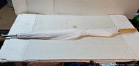 Full view of furled white umbrella showing wooden handle and chrome tip