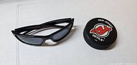 Pair of black wraparound sunglasses and New Jersey Devils hockey puck side by side