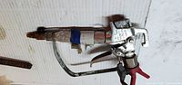 Left side view of complete airless paint spray gun showing tip, guard and trigger