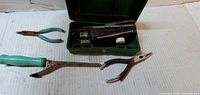 Open green case with Singer attachment, two pliers and curling iron visible