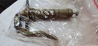 Full view of grease gun inside plastic bag showing lever handle