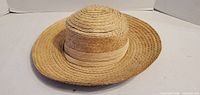Oblique view of brown woven straw hat showing brim and ribbon