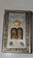 Front cover showing silver-plated embossing, brass crown and tablets, blue cabochons