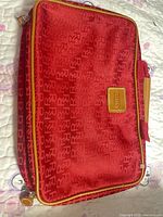 Front view of red Revlon monogram cosmetic bag with tan leather trim and zipper pulls