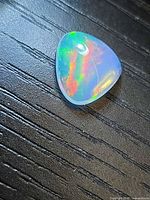 Trillion crystal opal on dark surface, showing multicolor flash and drilled hole