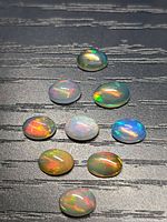 All nine oval cabochon opals on black textured surface