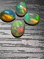 Four oval cabochon opals on black textured surface showing multicolour flashes
