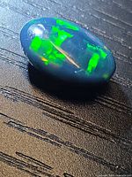 Oval cabochon opal showing bright green play-of-color on dark background