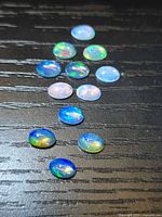 Triangular arrangement of 13 oval opals on dark surface