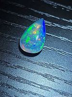 Pear cabochon opal on dark background showing multicoloured flash