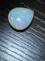 Pear-shaped opal showing multicolored flash pattern on black surface