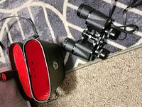 Binoculars beside open hard case showing red interior and neck strap