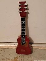 Front view of red and black mini guitar showing sound hole, fretboard and missing strings