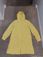 Front view of yellow hooded raincoat laid flat showing hood, pockets, front closure