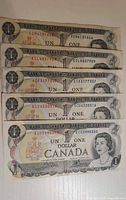 Obverse of five 1973 Canadian $1 bills stacked showing serial numbers and portrait