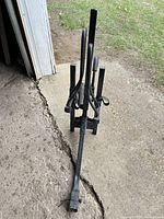 Front angled view of black steel hitch-mounted rack with vertical posts, wheel cradles and straps visible