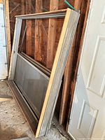 Stacked aluminum sliding door frames with screens leaning against wall