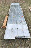 Stack of corrugated galvanized steel panels on pallets showing surface rust and dents