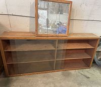 Front view of oak veneer bookcase with glass sliding doors and mirrored medicine cabinet placed on top
