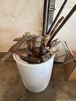 White barrel holding assorted sledges, axes and picks
