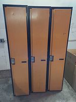 Front view of three orange single-tier lockers with black trim and lock handles