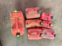 Seven red plastic gas cans of varying sizes with caps and spouts shown together