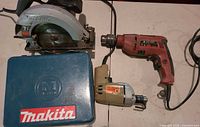 Top view of Skilsaw circular saw, two corded drills and Makita case on table