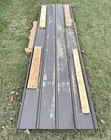 Stack of brown ribbed steel roof panels on grass with spacers