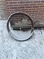 Rusted steel ring leaning against wall on snowy ground