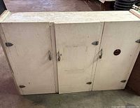 Front view of white plywood cabinet showing three doors with handles and hinges