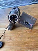 Front view of camcorder with flip-out LCD, lens cap nearby
