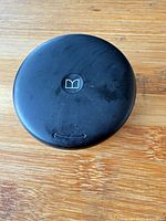 Closed black round charging case top view with Monster logo, shows scuffs