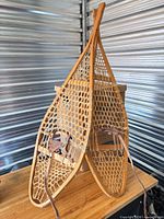 Full view of pair of wooden snowshoes standing upright on table