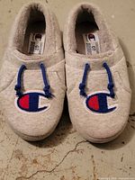 Top view of both slippers showing gray knit uppers, blue drawcords and Champion logo patches
