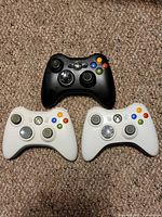 Top-down view of three Xbox 360 wireless controllers: two white, one black