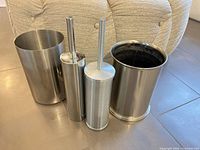 Four stainless steel bathroom containers: two wastebaskets and two toilet brush holders
