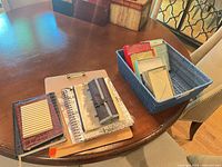 Full lot on table showing notebooks, journals, clipboard, pencil roll and basket of card sets