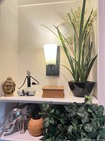 Shelf view of elephant figurine, round jar, faux ivy, Buddha head, abstract figure, black pot faux grass plant and decorative box