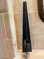 Full view of metal wall sculpture showing black backplate, bronze climber and spiral rope base