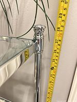 Top corner post of chrome etagere with measuring tape for height reference