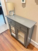 Front view of gray console cabinet showing drawers and glass doors