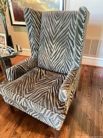 Front view of wingback chair showing zebra upholstery, arms, seat cushion, wooden legs