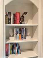 Shelf view with bronze hand sculpture centered between books and pair of white owl bookends below