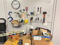Overall wall pegboard with hanging hand tools, levels, clamps, boxed items and cardboard boxes on table