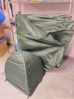 Two folded green polyethylene tarps leaning against shelving